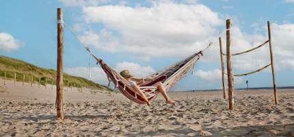 Eine Person mit Hut liegt in einer Hängematte am Strand.