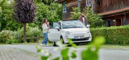 Familie mit Kleinkind steigt in ein Auto vor einem Haus.