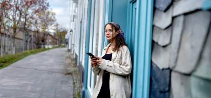 Junge Frau steht vor der blauen Tür eines Reihenhauses.