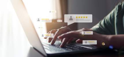 Eine Person schreibt etwas an einem Laptop. Im Vordergrund sind Bewertungen mit Sternen zu sehen.