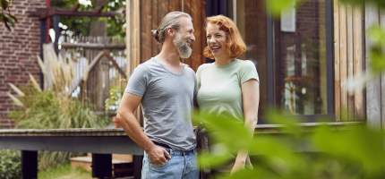 Ein Mann und eine Frau stehen glücklich vor ihrem Haus im Garten