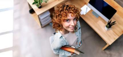Eine junge Frau steht vor ihrem Arbeitsplatz im Büro