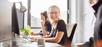 Eine Frau im Büro dreht sich lächelnd zu einer anderen Person.