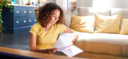 Eine junge Frau sitzt auf dem Boden und liest einen Brief.