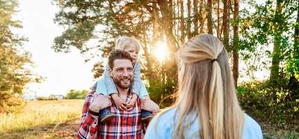 Eine Familie steht vor Bäumen und einem Feld.