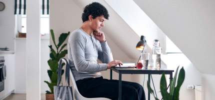 Ein junger Mann sitzt an einem Schreibtisch an seinem Laptop