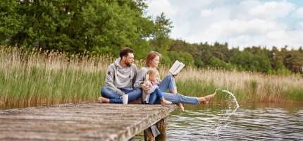 Eine Familie sitzt gemeinsam auf einem Steg und hält die Füße in den See.