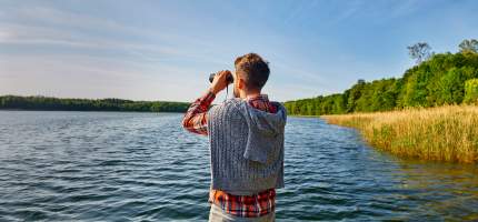 Mann mit Fernglas schaut auf den See.