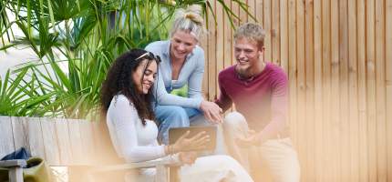 Eine Gruppe junger Menschen sitzt draußen auf einer Bank und schaut auf ein Tablet.