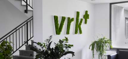 Ein großes begrüntes Logo vom Versicherer im Raum der Kirchen an einer Wand
