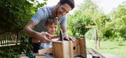 Ein junger Vater baut mit seinem Sohn ein Vogelhaus.