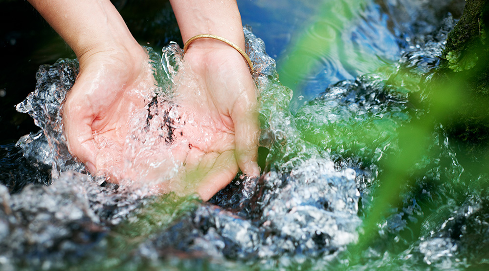 Hände greifen in einen Flusslauf.