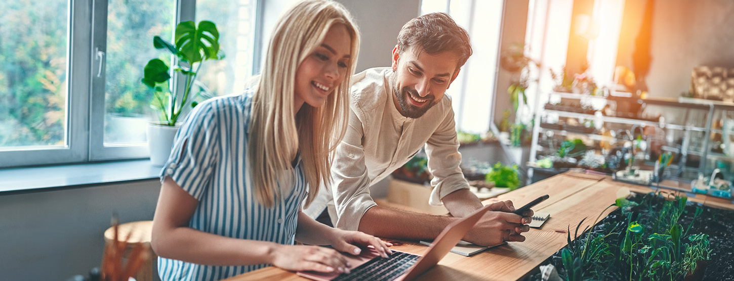 Eine Frau arbeitet an einem Laptop, ein Mann schaut auf den Bildschirm. 