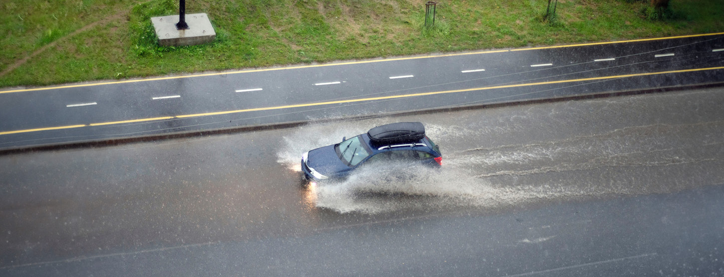 Ein Auto fährt auf einer überschwemte Straße.