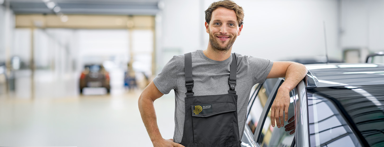Ein Mechaniker steht neben einem Auto in einer Werkstatt.