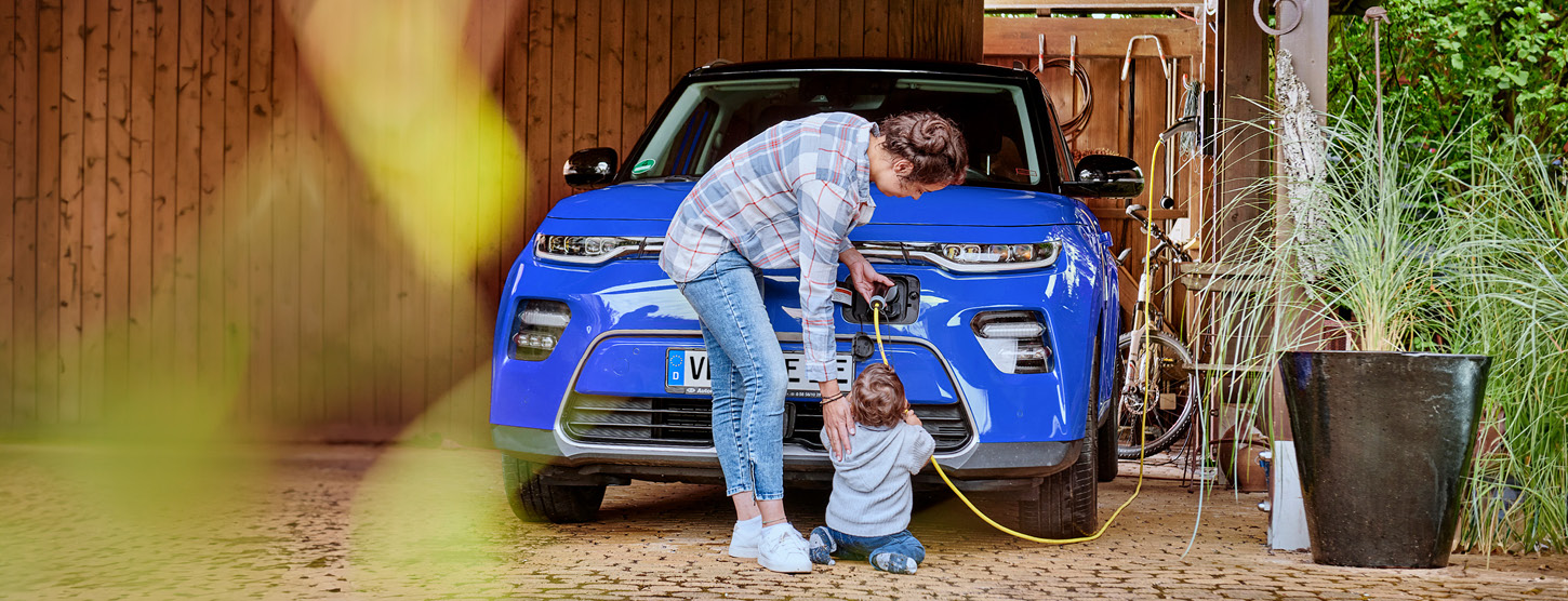 Eine Frau lädt ihr Elektroauto auf. Ihr kleines Kind hilft und hält das Kabel.