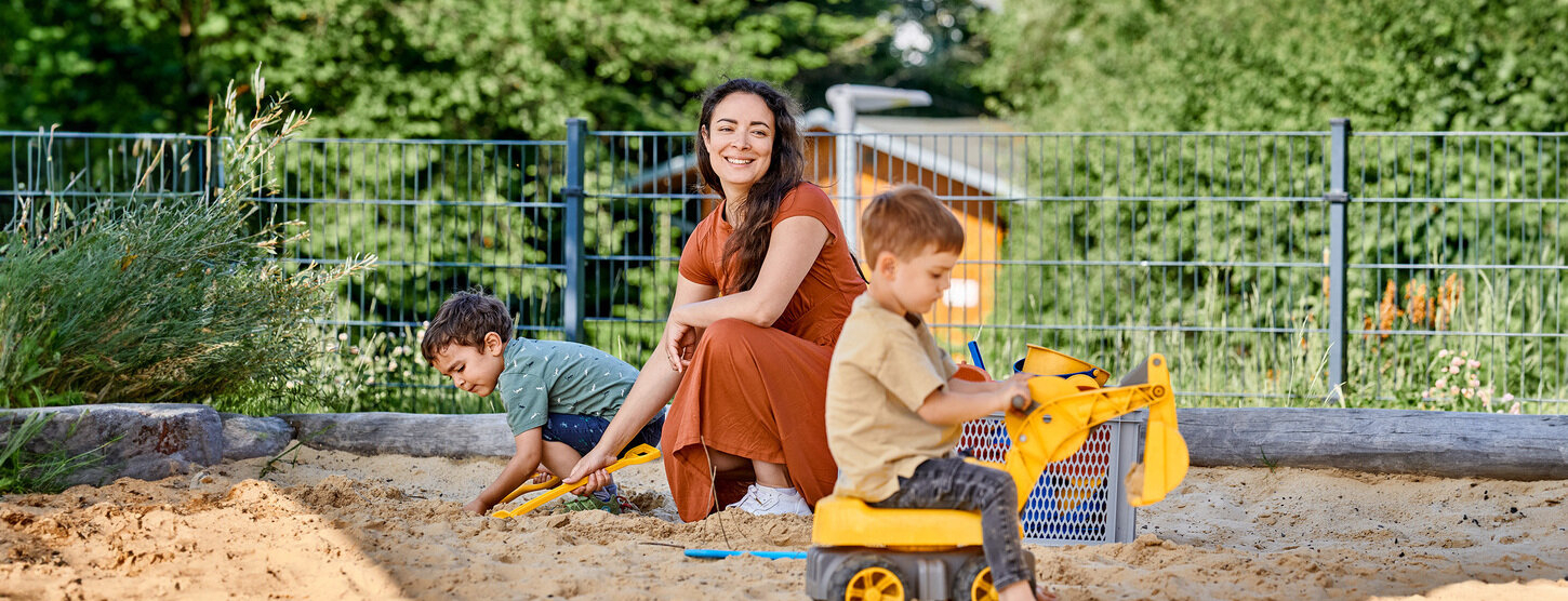 Eine Frau spielt mit zwei Kindern im Sandkasten.