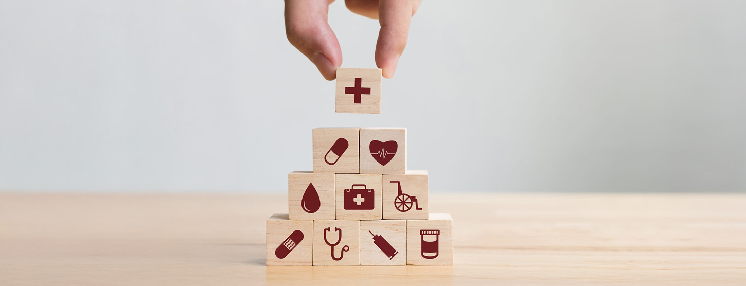 Eine Hand stapelt Holzklötzchen mit Grafiken aus dem Gesundheitswesen.