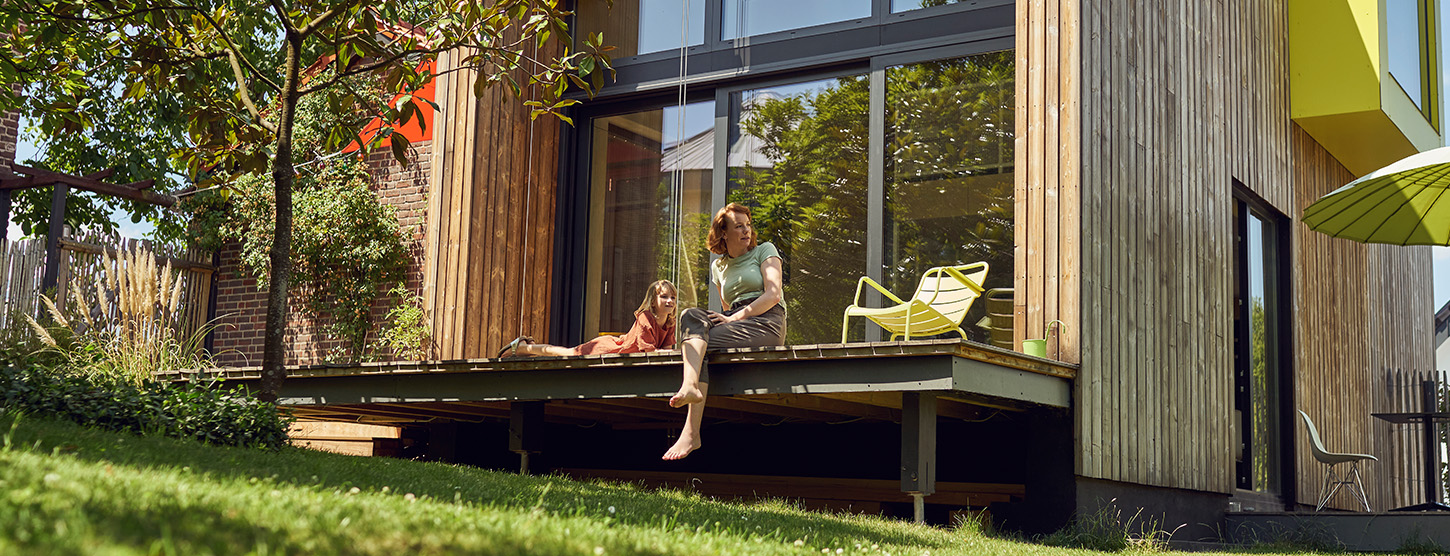 Eine Mutter sitzt mit ihrer kleinen Tochter auf der Terrasse und schaut in den Garten.