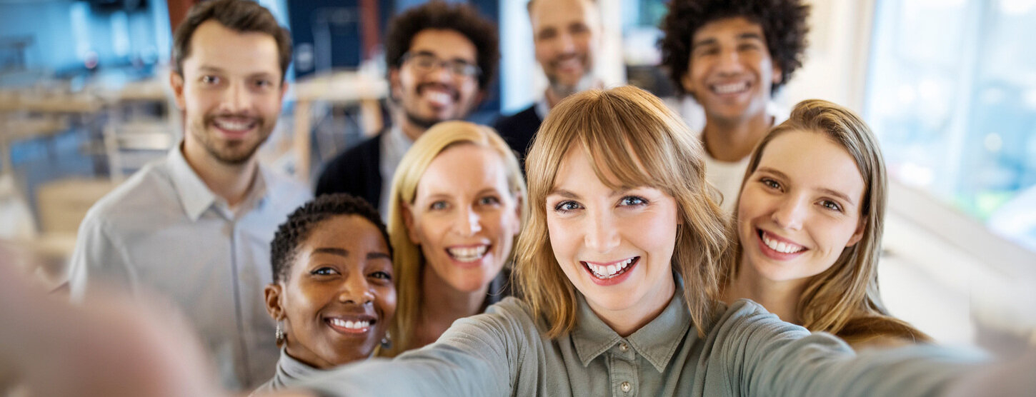 Acht Personen machen ein Selfie. Eine Frau hält die Kamera mit beiden Händen.