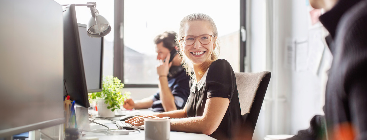 Eine Frau im Büro dreht sich lächelnd zu einer anderen Person.