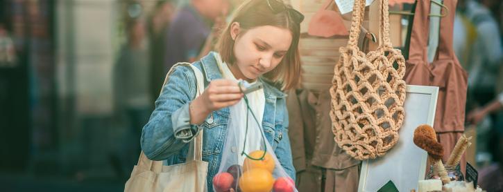 Eine Frau kauft Gemüse auf dem Markt mit einer Jutetasche.