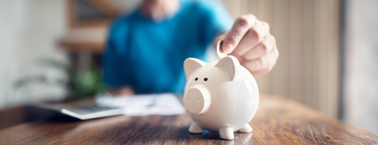 Eine Person wirft Geld in ein Sparschwein.