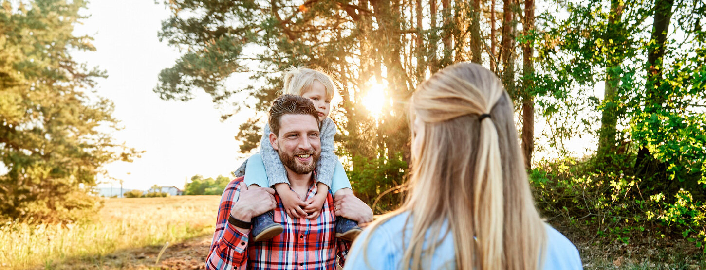 Eine Familie steht vor Bäumen und einem Feld.