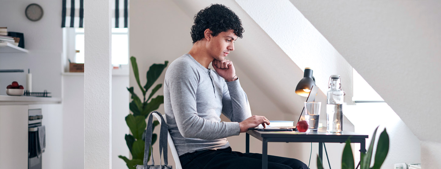 Ein junger Mann sitzt an einem Schreibtisch an seinem Laptop