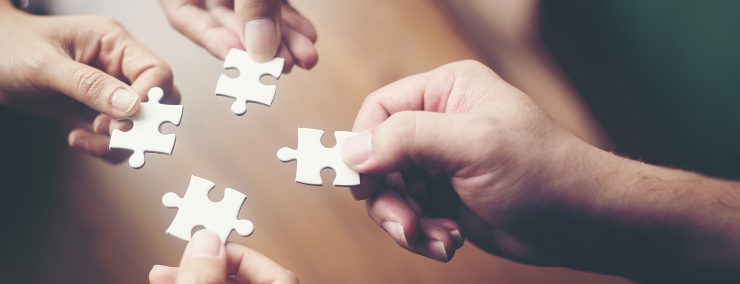Vier Hände halten jeweils ein Puzzleteil in die Mitte.