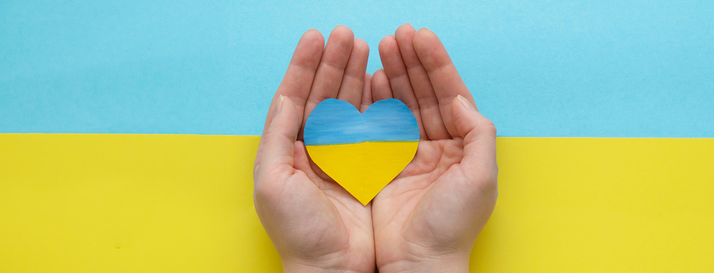 Hände halten ein Herz in ukrainischen Farben vor dem Hintergrund der ukrainischen Flagge.