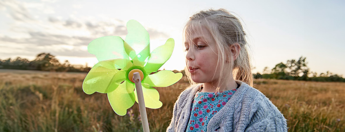 Ein Mädchen pustet in ein Windspiel.