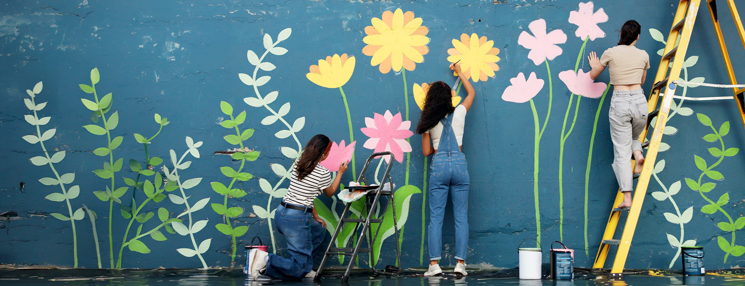 Eine Gruppe Menschen malt bunte Blumen an eine Wand.