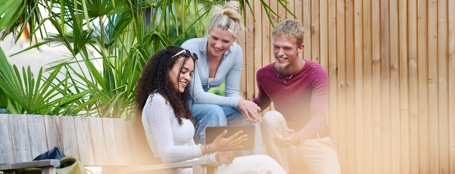 Eine Gruppe junger Menschen sitzt draußen auf einer Bank und schaut auf ein Tablet.