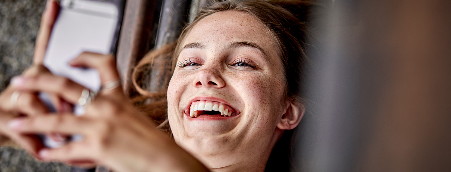 Eine junge Frau schaut auf ihr Handy und ist glücklich.