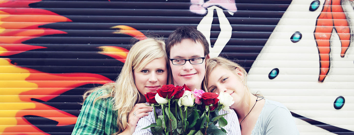 Zwei Frauen stehen neben einem Mann, er hält einen Strauß Rosen.