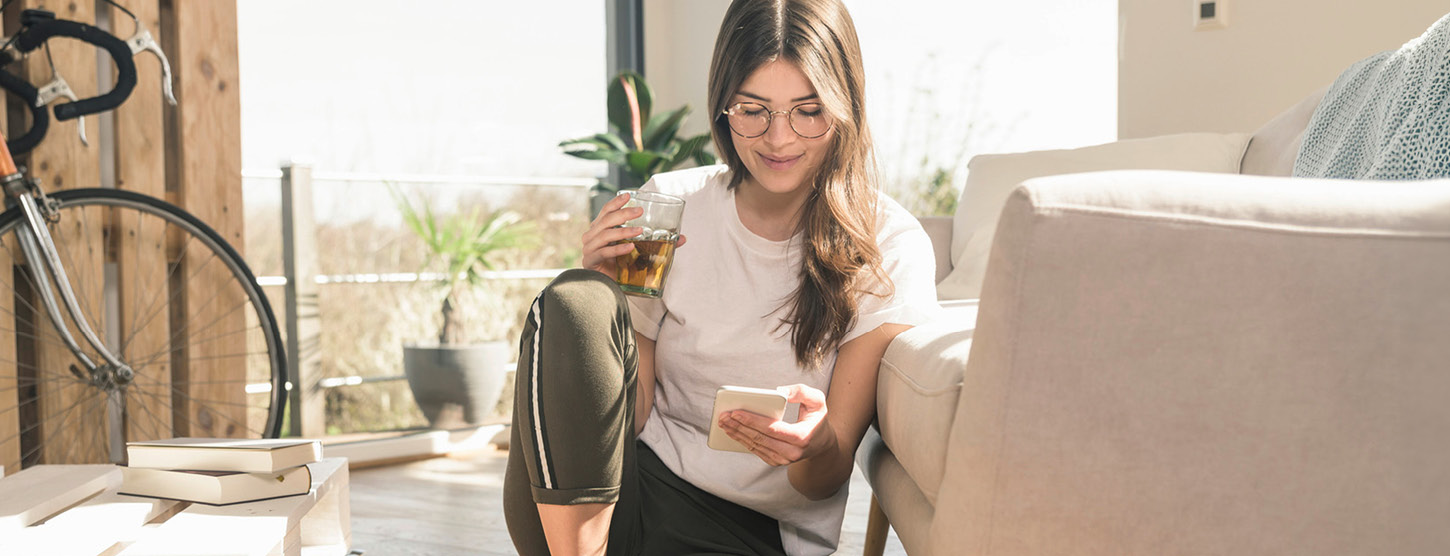 Frau sitzt auf dem Boden und schaut auf ihr Handy.