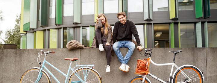 Ein Mann und eine Frau sitzen auf einer Mauer vor der Fahrräder stehen.