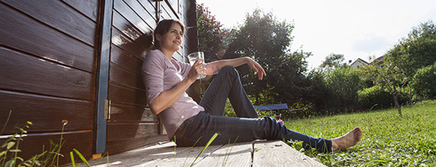 Eine junge Frau sitzt entspannt in der Sonne im Garten.