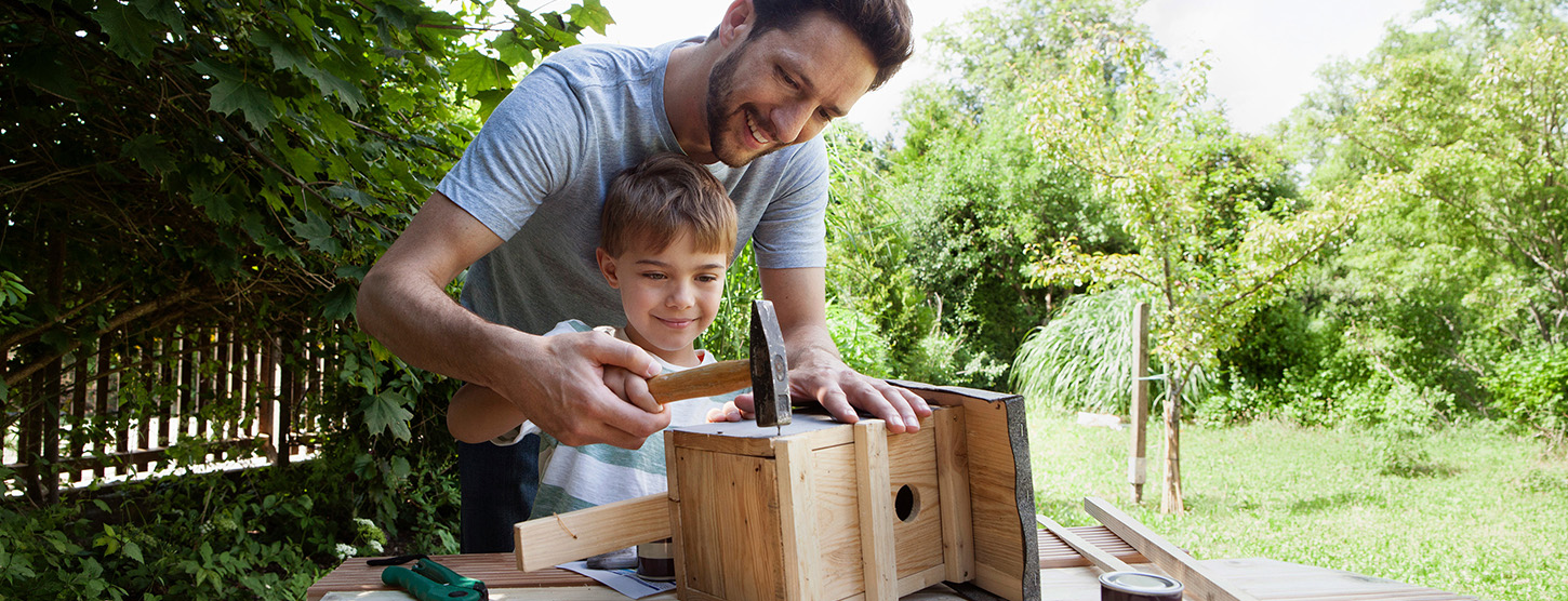 Ein junger Vater baut mit seinem Sohn ein Vogelhaus.