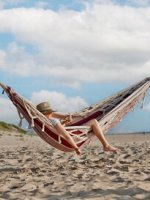 Eine Person mit Hut liegt in einer Hängematte am Strand.