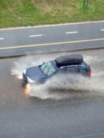 Ein Auto fährt auf einer überschwemte Straße.