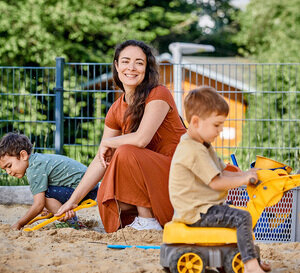 Eine Frau spielt mit zwei Kindern im Sandkasten.