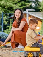 Eine Frau spielt mit zwei Kindern im Sandkasten.