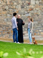 Ein Mann und eine Frau sprechen mit einem Pfarrer vor einer Kirche mit dem Hund an der Leine.