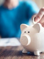 Eine Person wirft Geld in ein Sparschwein.