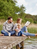 Eine Familie sitzt gemeinsam auf einem Steg und hält die Füße in den See.