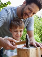 Ein junger Vater baut mit seinem Sohn ein Vogelhaus.