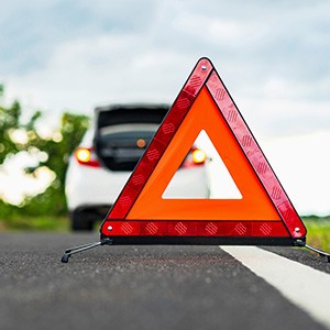 Ein Warndreieck auf einer Straße im Hintergrund ist ein Auto zu sehen.