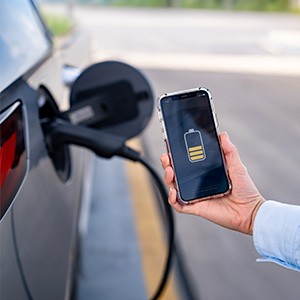 Eine Hand hält ein Handy mit einer Ladeanzeige des E-Autoakkus.